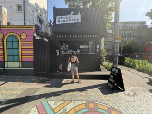 From sidewalk facing venue. Kiosk on back. A-framed sign on right.