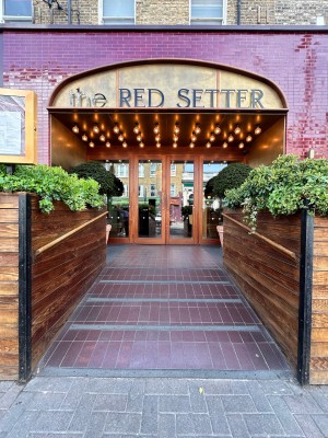 From street facing venue. Opening ahead with built in ramp up to entrance at back. Wooden handrails along left and right.