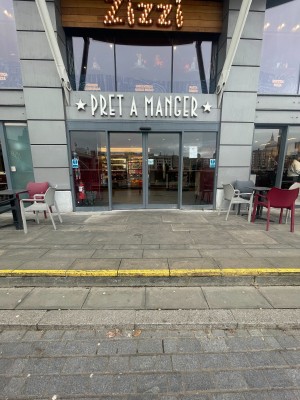 Facing entrance. Two steps up before entrance. Grey framed glass doors ahead. Outdoor seating on both sides.