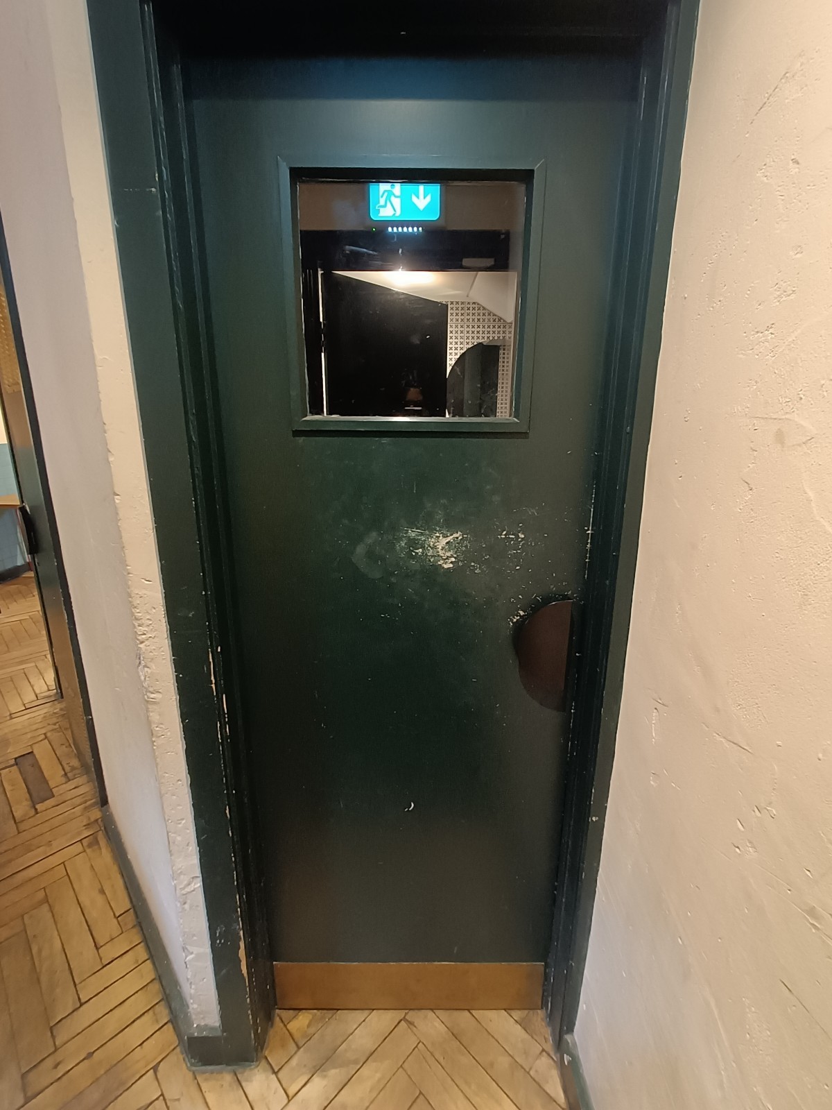 From in front of bathroom, facing left. Green wooden door ahead. Push from right to open.