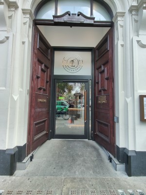 Brown wooden preceding doors. Push from centre to open. Doorbell for assistance on left.