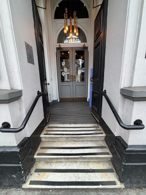 Three steps up to black doors. Push from centre to open. Black handrails on either side.