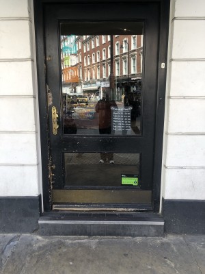 Glass door with black frame. Push handle on left to open.