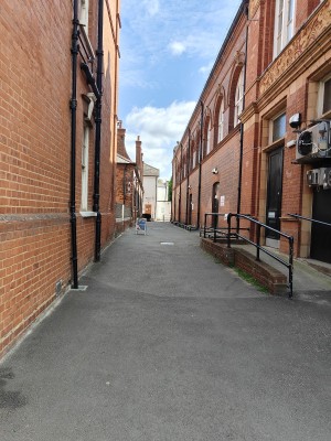 From right of main building facing straight. Path ahead to A-frame sign at back left. Preceding entrance door behind.