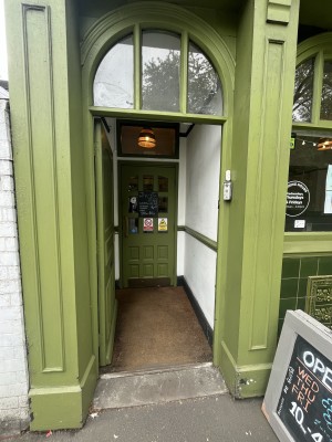 Green wooden door ahead. Push gold handle on right to open. White doorbell to right of door.