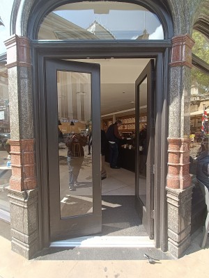 Glass door with black, wooden frame. Push from middle to open.