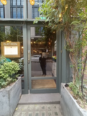 Glass door with green wooden door ahead. Push golden handle on left to open.