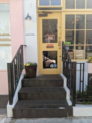 Three dark grey steps up with metal handrails along both sides. Yellow door with glass panel at top of steps. Push from metal handle on right to open.