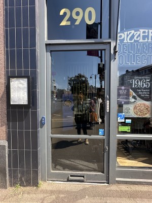 Glass door with grey frame ahead. Push from right to open. Doorbell for assistance left of door.