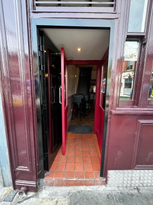 Black door in maroon frame ahead. Push from right to open.
