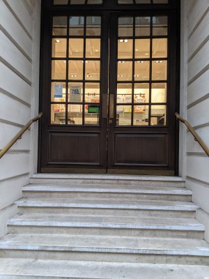 Stairs with metal handrail on both sides leading to glass and wood doors with white frame and metal handles in centre. Push to open.