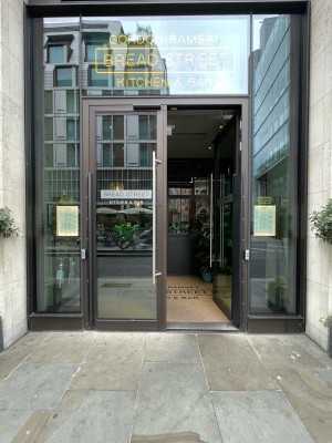 Facing entrance. Metal framed glass doors ahead. Silver vertical handles at centre. Push button on right side of frame to open.