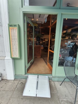 Ramp upon request up to green framed glass door. Push metal handle on right to open.