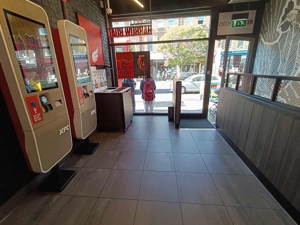 From counter, facing back right. Ordering screens along left. Bins behind. Steps to doorway at back right.