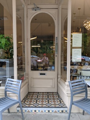 Glass door with beige frame and metal handle on right. Pull to open.
