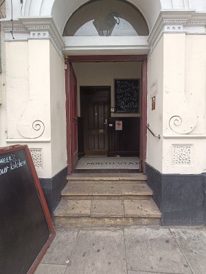 From entrance, facing right. A-frame board on left. Steps up to brown wooden doorway at back. Push from middle to open.