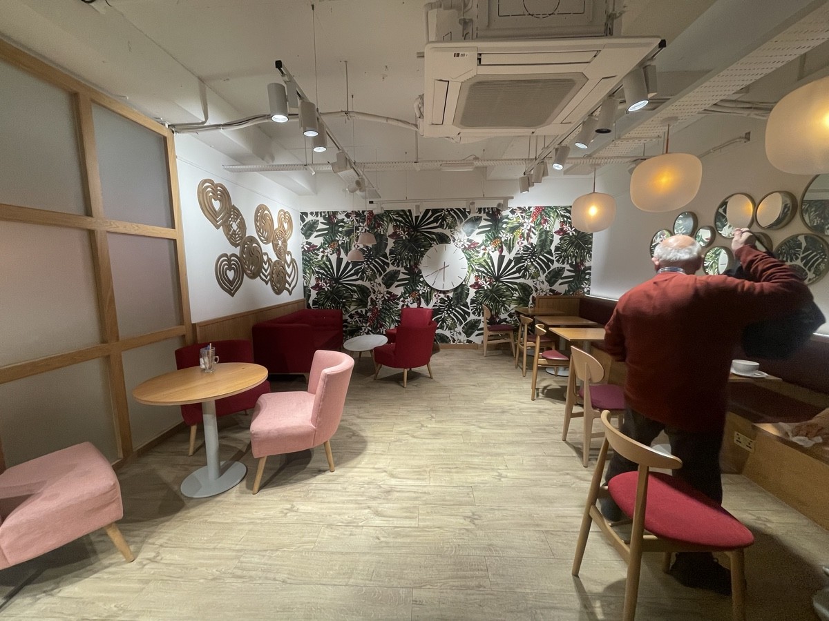 From bottom of stairs facing right. Armchairs, couch and tables along left. Half booths and chairs along right.