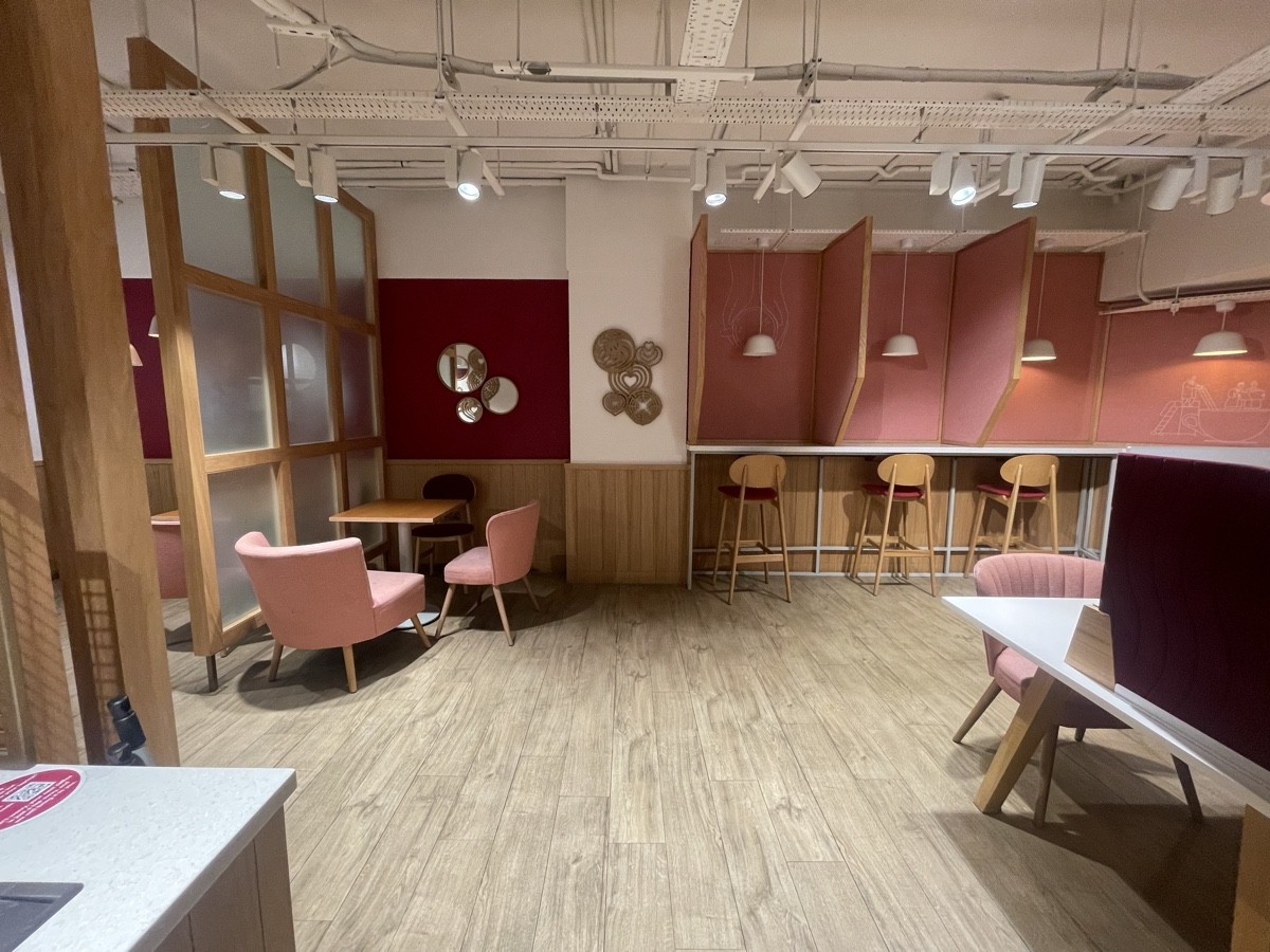 From opening facing straight. Armchairs and tables at back left. High table and stools with dividers in between along back right.