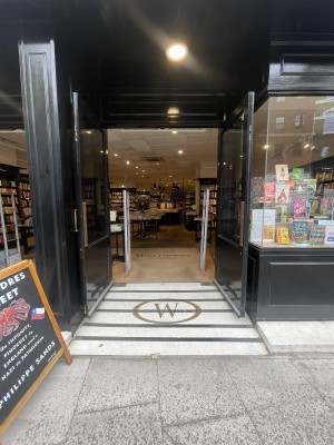 Black glass and wooden doors ahead. Pull gold metal handles from centre to open. Second set of doors to its left.
