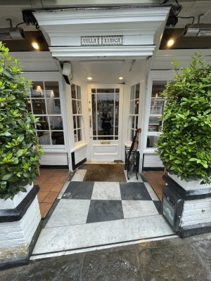 From street facing venue. Opening ahead with planters on both sides. Outdoor seating to left and right after opening. Entrance door at back.
