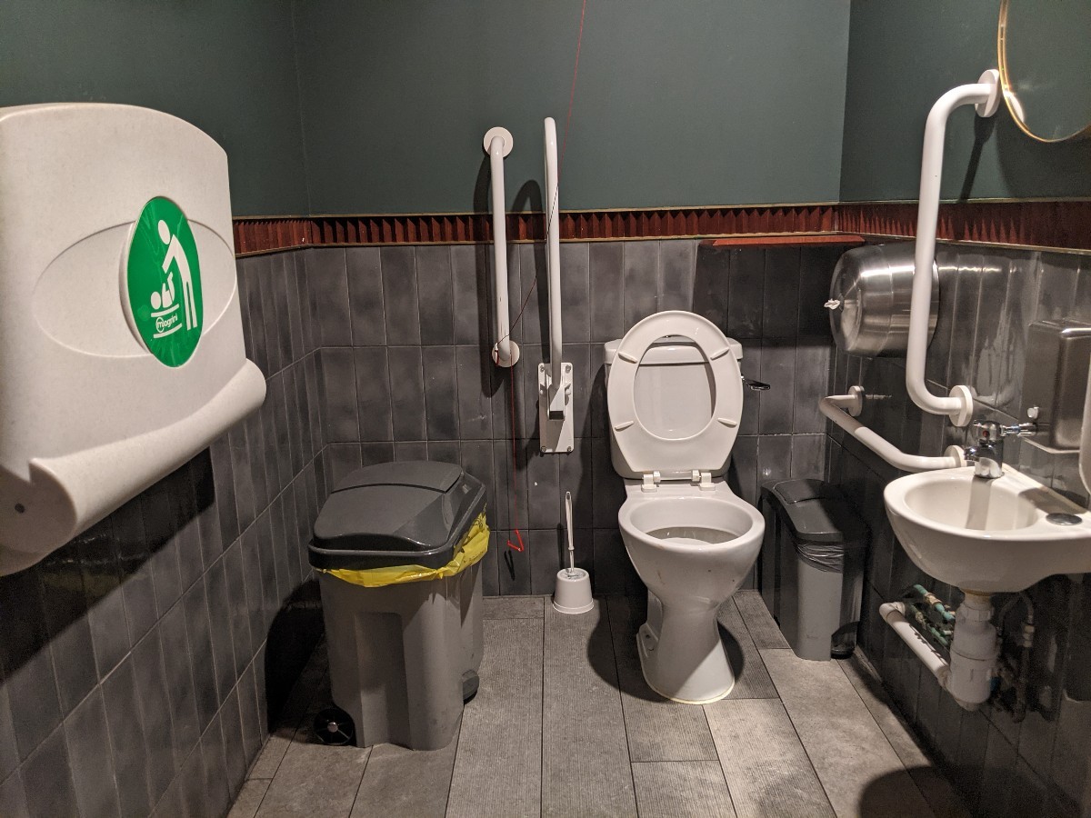 From door facing straight. Sink on right. Toilet back right, emergency pull cord left of toilet. Baby change table on left wall.