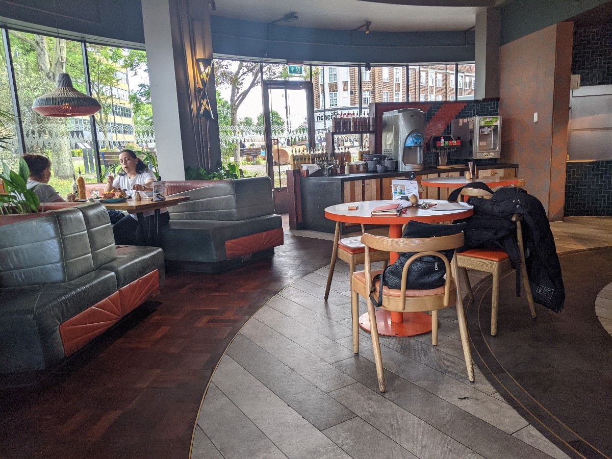 From end of counter facing straight. Booths along left, tables with chairs ahead. Condiment station at back.