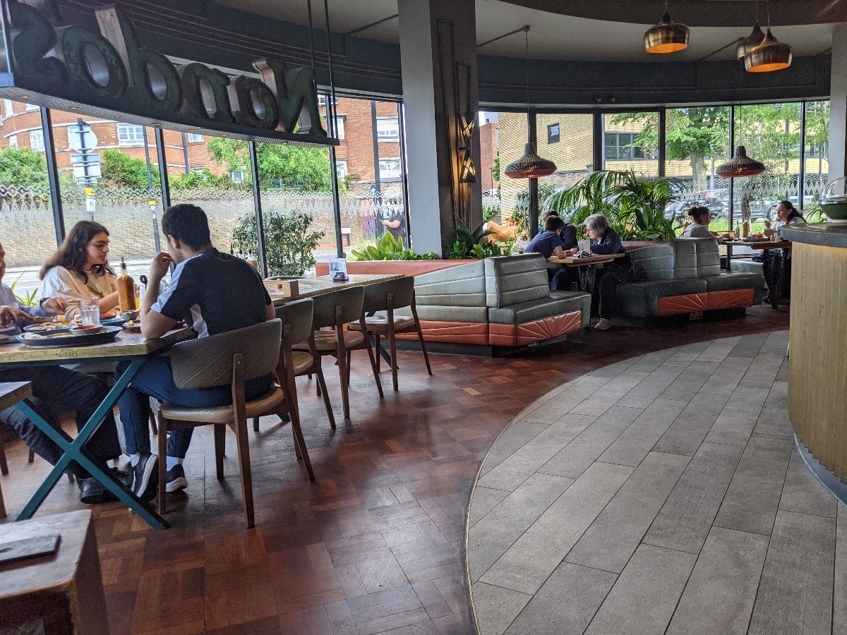 From after entrance facing left. Tables with chairs on left. Booths at back. Counter along right.