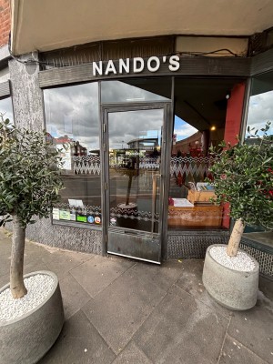 From sidewalk facing venue. Two planters ahead. Glass door with metal frame on back. Pull via handle on right to open.