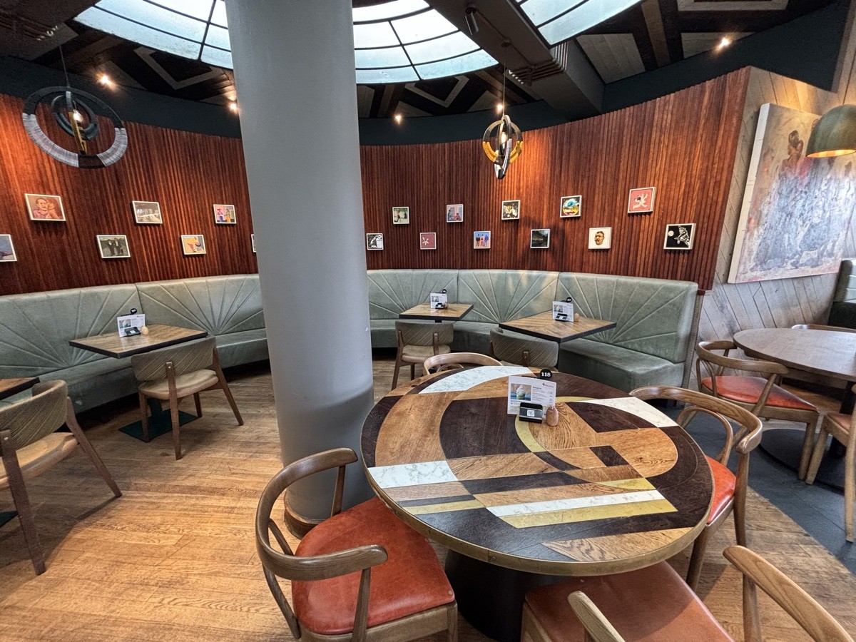 From divider facing straight. Tables on right and  ahead. Column in center. Half booth along left and back.