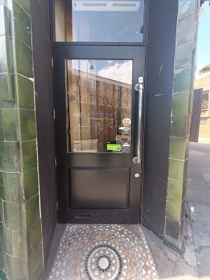 Glass door with black, wooden door ahead. Pull silver handle on right to open.