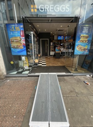 Ramp upon request to glass doors. Push silver handles in centre to open. Doorbell for assistance on left of doors.