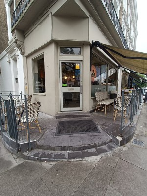 From street, facing venue. Opening ahead. Outdoor seating on either sides. Doorway at back.