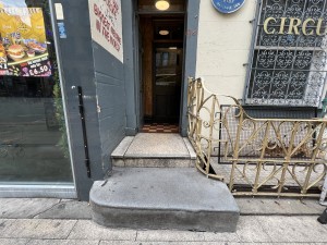 2 steps up to blue door. Push from right to open. Metal handrail along right.