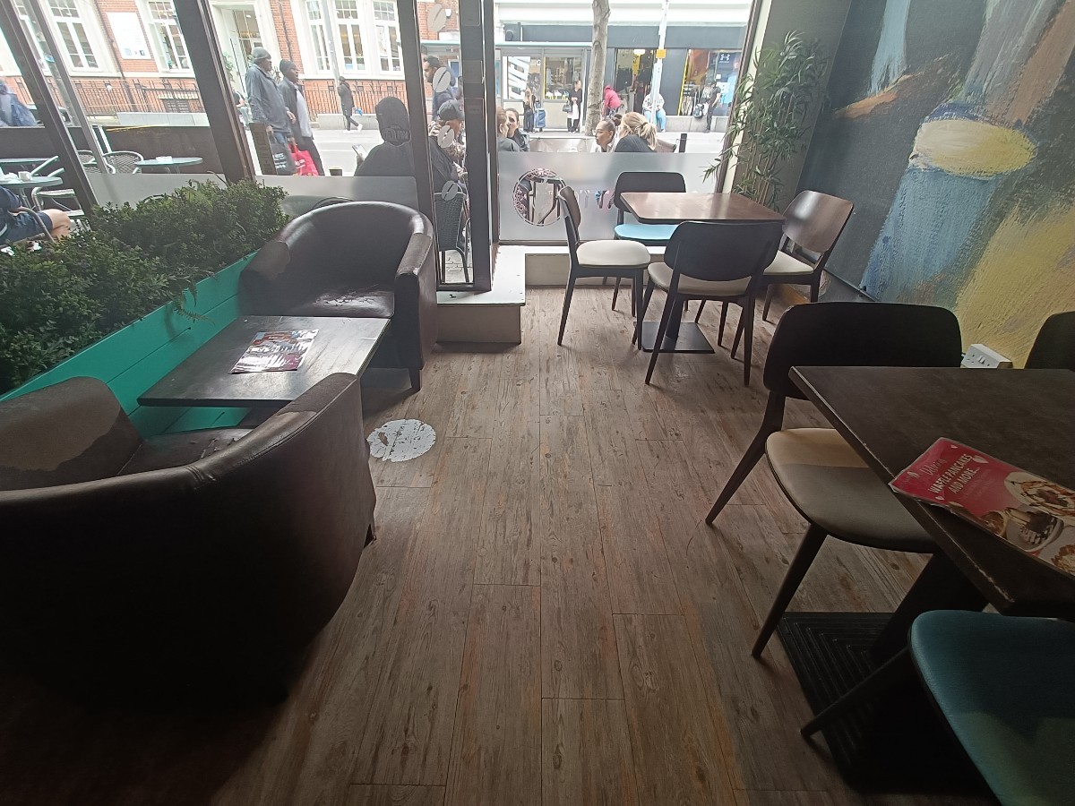 From after planter, facing left. Table and armchairs on left. Tables and chairs along right.