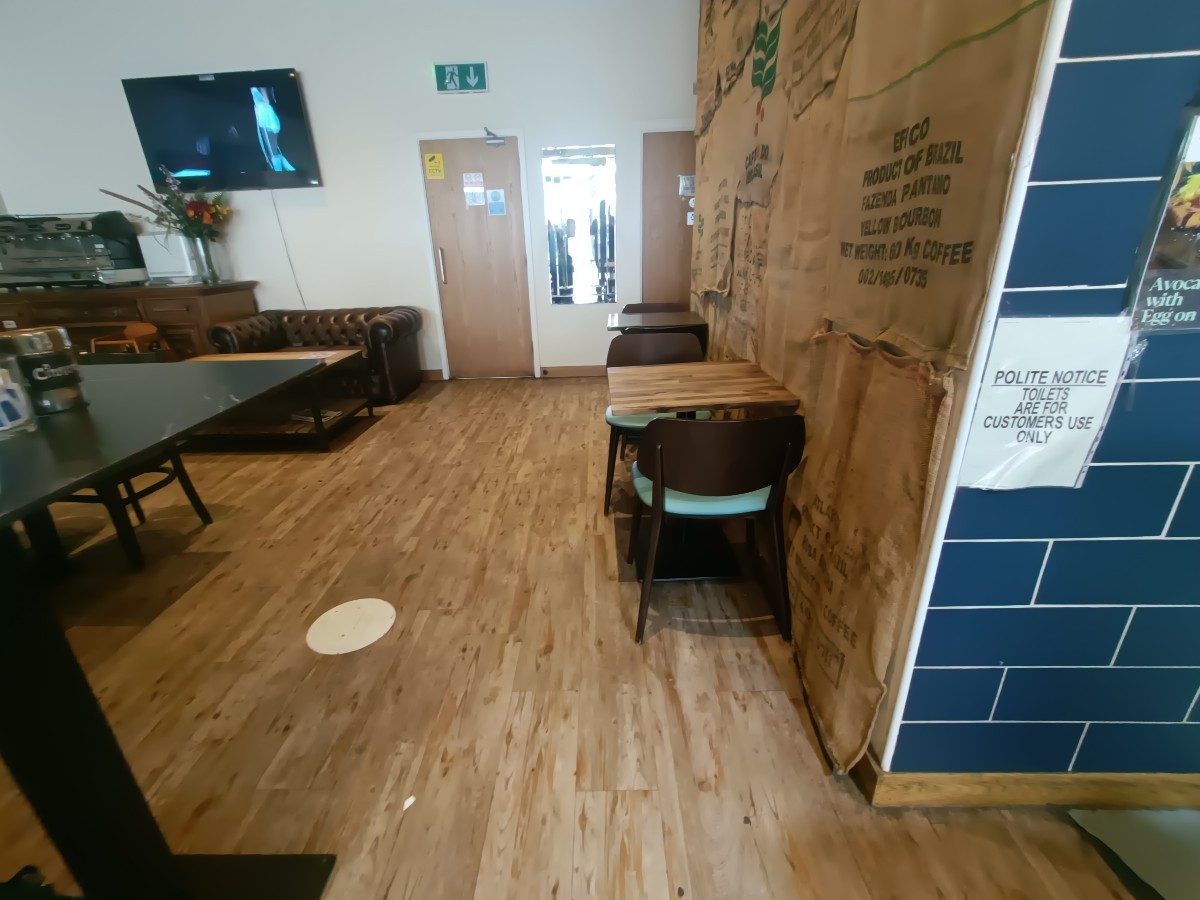 From end of counter, facing straight. Condiments station on left. Table and chairs on right. Bathroom behind.