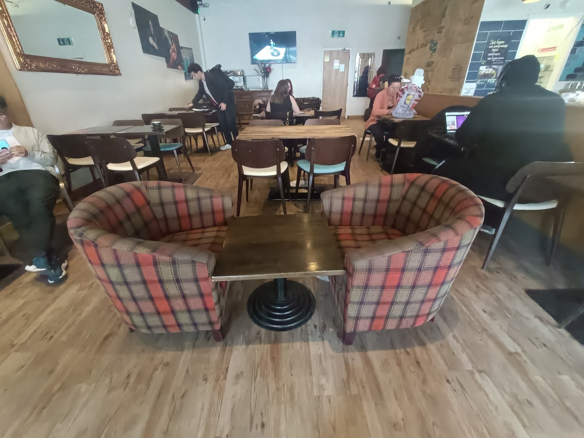 From after planter at entrance, facing right. Table and armchair ahead. Tables and chairs behind and along both sides.