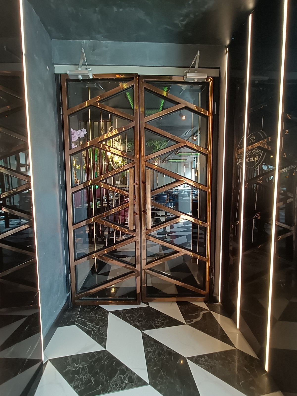 From left of wall divider, facing straight. Glass door with golden metal frame ahead. Pull golden handles in middle to open.