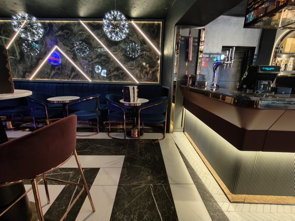 From beginning of bar facing right. High tables and stools on left. Half booth along back wall.