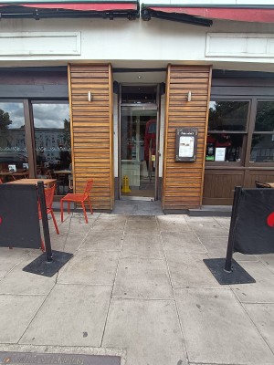From street, facing venue. Restaurant barriers on both sides. Outdoor seating behind. Doorway at back.