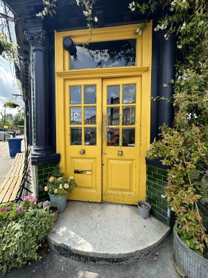 Yellow and glass panelled doors. Push from centre to open. Planters to left and right of it.