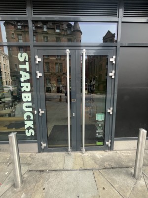 Glass doors with black frame. Pull silver handles in centre to open. White doorbell to left of doors. Silver bollards to left and right.