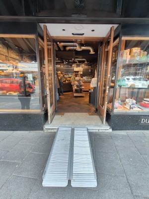 Ramp upon request to first set of brown framed glass doors. Pull golden handles in centre to open.
