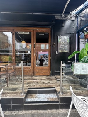 From pavement facing venue. Opening ahead. 2 steps up at foot of it. Glass dividers to left and right of opening.
