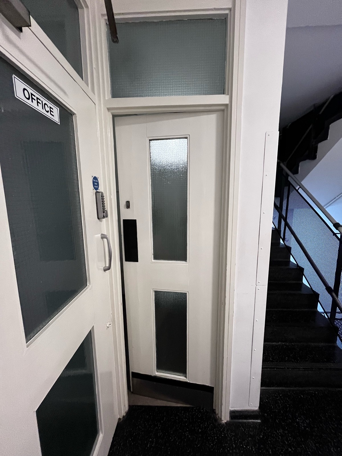 From staff door facing right. White and glass panelled preceding door. Silver pad on left, push to open.
