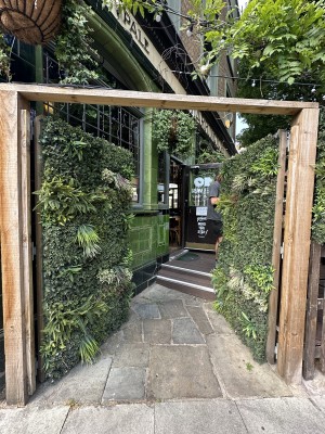 From pavement facing venue. Wooden gates ahead. Push from centre to open.