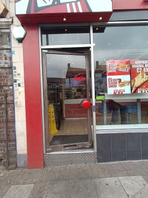 Glass door with brown metal frame. Push red handle on right to open. Doorbell on right doorframe.