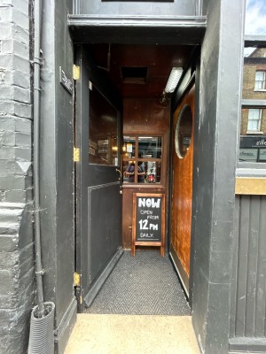 Black wooden door with glass panel. Push gold handle on right to open.