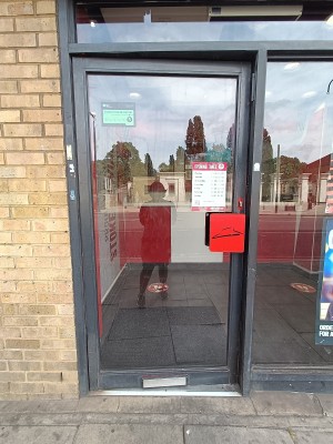 Glass door with black metal frame ahead. Push red handle on right to open.