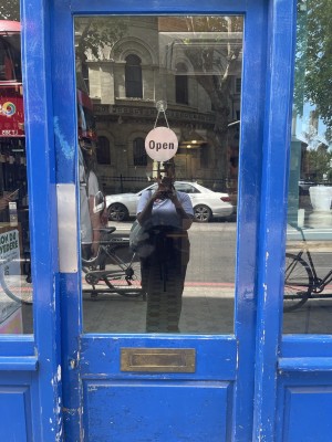 Facing glass door with blue frame. Push on left to open.