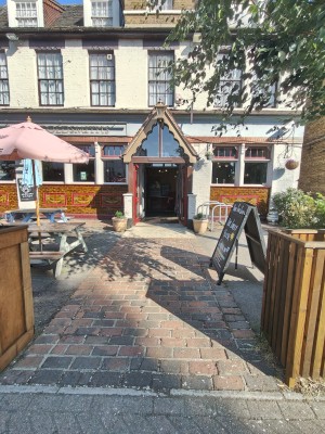 From street facing venue. Cobbled path ahead to entrance at back. Outdoor seating on left. Planters on left and right.